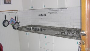Ett kök med vita skåp, en bänkskiva i granit, en dubbel diskho och en gasspis.