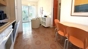 A modern kitchen with a dining area, a view through the glass door, and a framed artwork on the wall. - Bright villa with a fenced garden near the beach (Bibione Pineda)