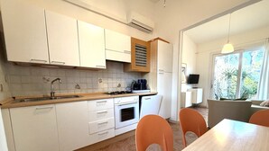 A modern kitchen with white cabinets, a stove, and a sink. There is a dining area with orange chairs and a table. - Bright villa with a fenced garden near the beach (Bibione Pineda)