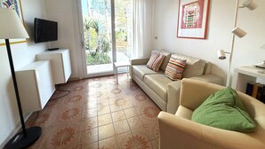 A living room with a sofa, a television, a table, and a door leading to a balcony. - Bright villa with a fenced garden near the beach (Bibione Pineda)