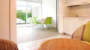 Habitación con comedor que incluye una mesa y sillas, cocina con armarios y vista a través de una puerta de cristal a un área de estar al aire libre.