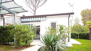 Una casa moderna con fachada blanca, un porche cubierto y un césped bien cuidado con arbustos variados y una planta de agave grande.