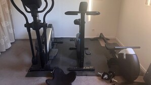 Ein Heimfitnessraum mit Crosstrainer, einer Hantelbank und einem Ergometer.