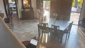 Ein geräumiger Essbereich mit einem großen Tisch und Stühlen, ein Laptop auf einem Holztisch und ein Blick ins Freie durch ein großes Fenster.