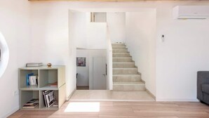 Eine Treppe führt zu einer oberen Etage, ein kleines Bücherregal und ein graues Sofa befinden sich in einem modernen, minimalistischen Wohnraum.
