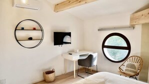Ein Schlafzimmer mit einem Bett, einem Schreibtisch, einem Sessel, einem Fernseher, einem runden Spiegel und einem Fenster.
