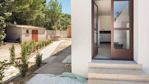 Ein modernes Haus mit einer Holterrasse, einem kleinen Garten und einer Glastür zur Küche.