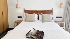 Een netjes opgemaakt bed met een geweven hoofdbord, twee nachtkastjes en een bedlampje.