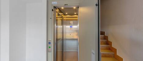 An elevator with a control panel, a staircase with a sign, and a wall with a bulletin board.
