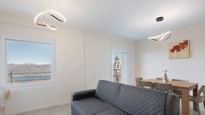 A modern living room with a gray sofa, a dining table with chairs, a view of mountains through a large window, and a painting on the wall. - Giulio's Apartment First Floor (San Zeno di Montagna)