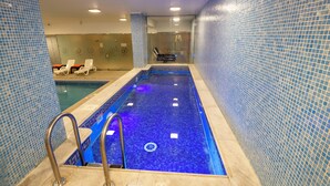 Una piscina con piastrelle blu a mosaico, un recinto in vetro e sedie a sdraio.