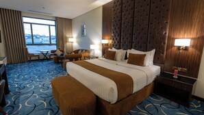 Camera d'albergo con un letto grande, una scrivania, una sedia e vista sulla città da una finestra ampia.