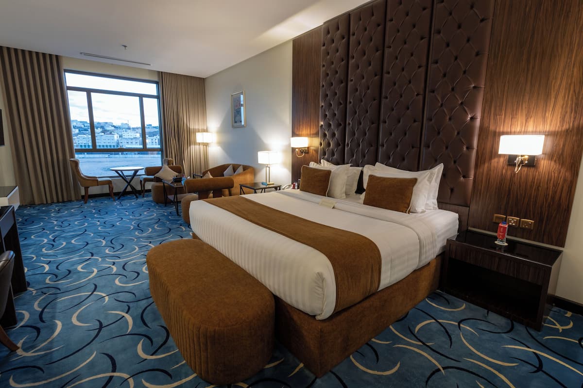 Habitación de hotel con una cama grande, un escritorio, una silla y vistas a la ciudad a través de un ventanal.