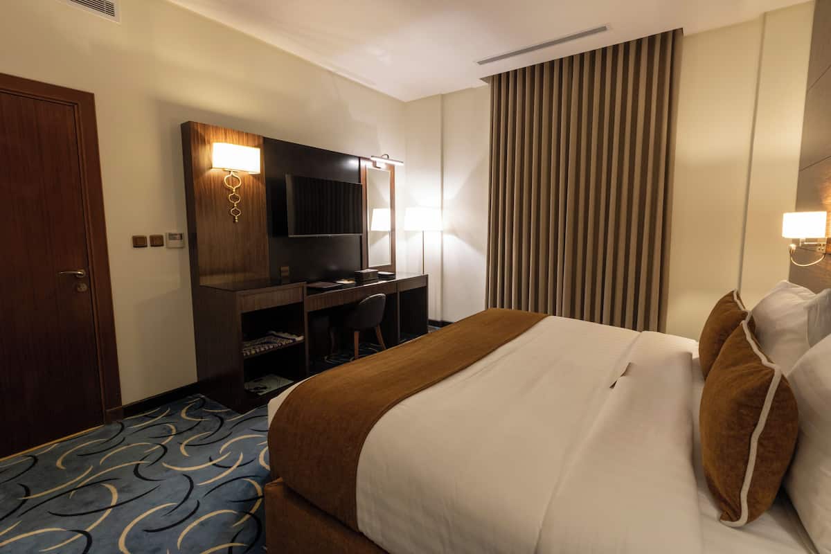 Una habitación de hotel con cama, escritorio, televisor y un gran ventanal con persianas.