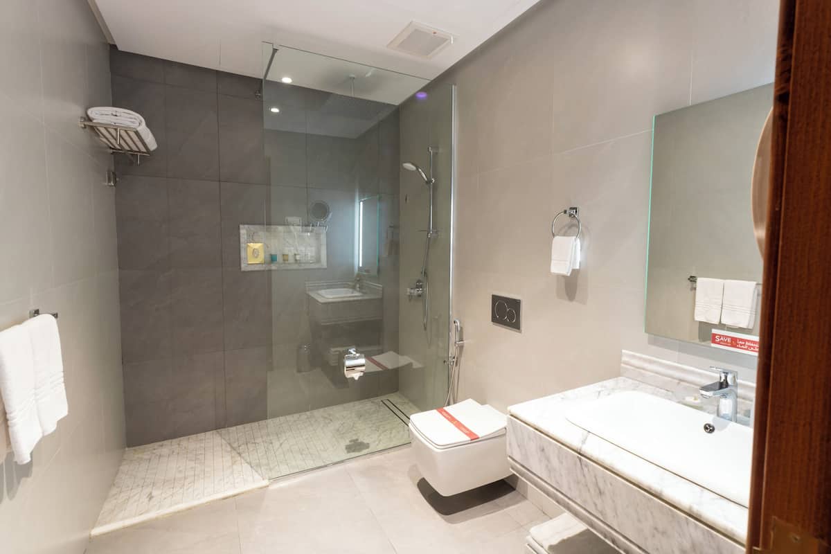 Un baño moderno con ducha envuelta en vidrio, lavamanos de mármol y un espejo grande.