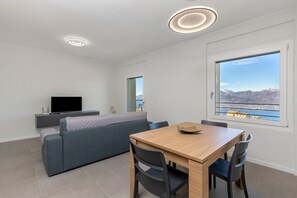 Uma sala de estar moderna com sofá, TV, mesa de jantar, cadeiras e uma grande janela com vista para as montanhas.