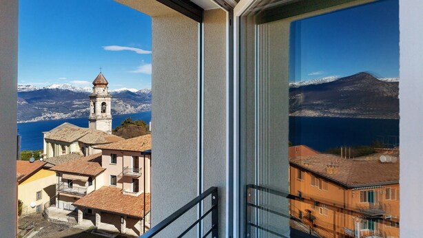 Vista desde un balcón que domina un pueblo costero con una torre de iglesia y montañas al fondo.