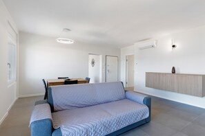 Uma sala de estar moderna com um sofá, uma mesa de jantar com cadeiras, um armário fixado na parede e um lustre.