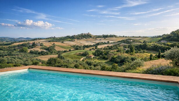 Une piscine entourée d’une terrasse en bois, avec une végétation luxuriante et des collines verdoyantes en arrière-plan.