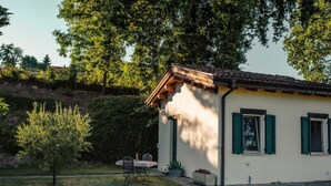 Une petite maison avec un toit en tuiles, une terrasse avec une table et des chaises, et un petit arbre au premier plan.