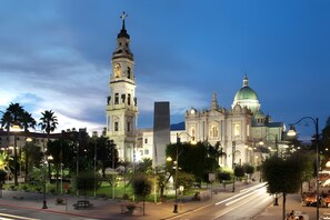 Una chiesa imponente con un campanile e una cupola ben visibili, circondata da una piazza illuminata, alberata e dotata di panchine.