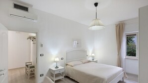 Ett sovrum med en säng, sängbord, en hängande lampa, ett fönster med gardiner och en luftkonditioneringsanläggning.