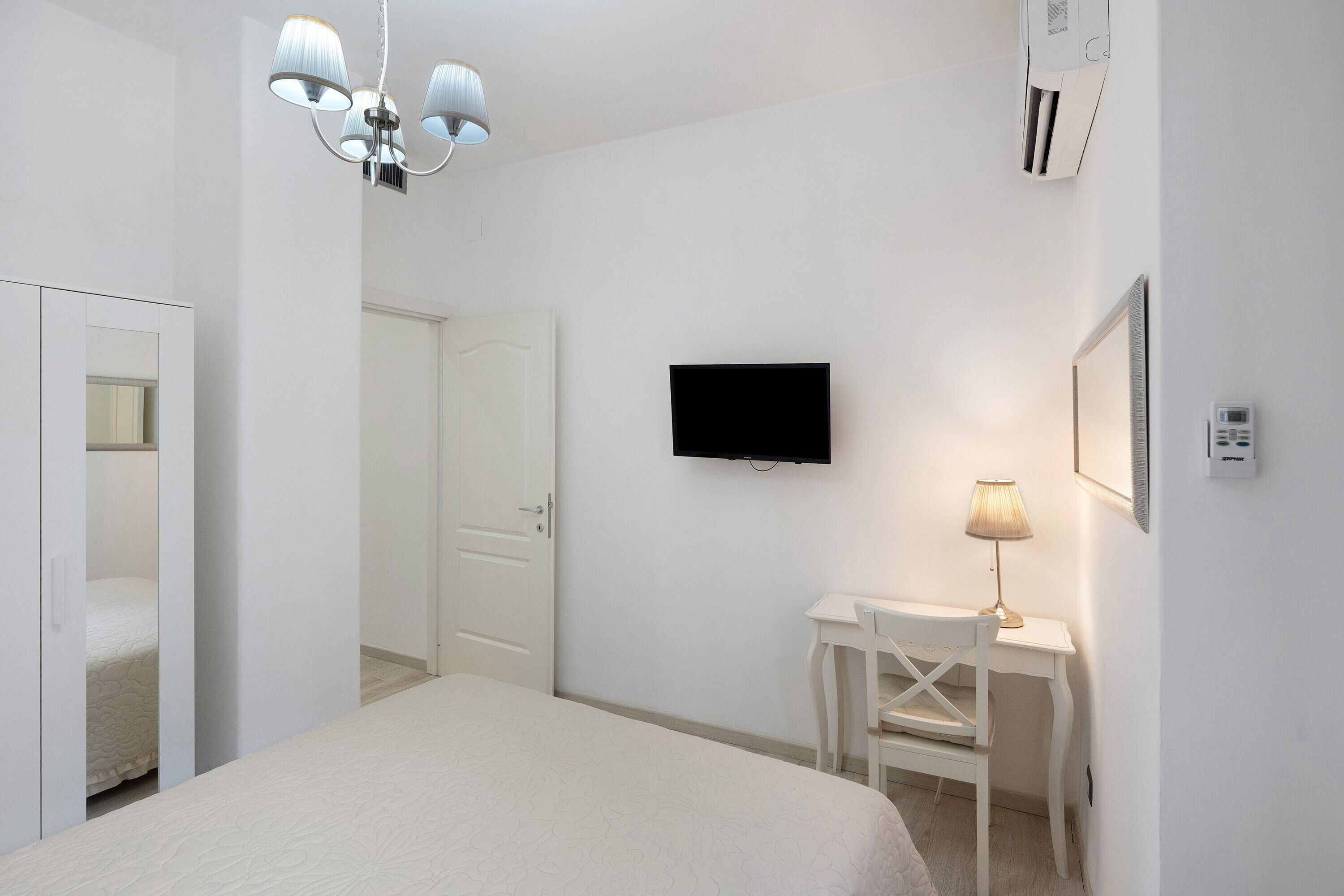A bedroom with a bed, a desk, a chair, a television, and a lamp.