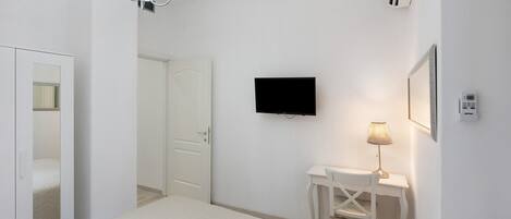 A bedroom with a bed, a desk, a chair, a television, and a lamp.