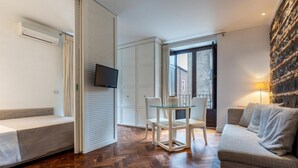 A hotel room with a sofa, a dining table with chairs, a TV mounted on the wall, and a large window. - GuestHost - A comfortable and welcoming 39 square meters studio apartment, perfect for two people, located on the second floor of a building with an elevator (NOT accessible to disabled guests).The property, located on a pedestrian street, enjoys a centr (Catania)