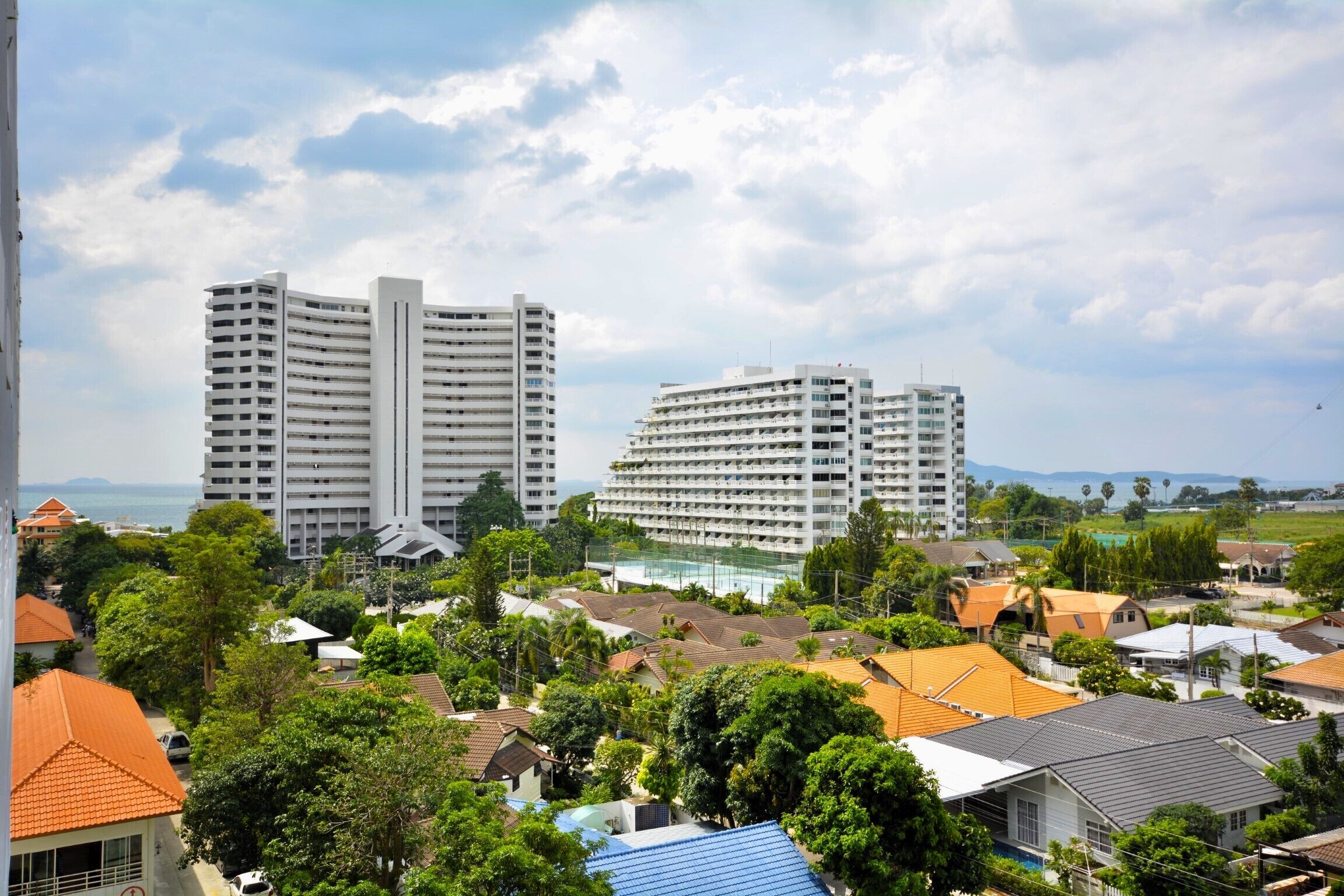 A coastal cityscape with two prominent white high-rise buildings, surrounded by lush greenery and smaller residential buildings.