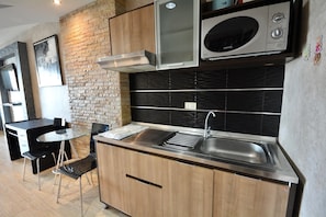A modern kitchen with a stainless steel sink, wooden cabinets, a black backsplash, and a brick wall. - Sea-view Studio With Large Balcony - View Talay 5D (Pattaya)