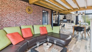 Ein modernes Wohnzimmer mit Backsteinwand, Holzboden und einem Sofa mit grünen und roten Kissen.