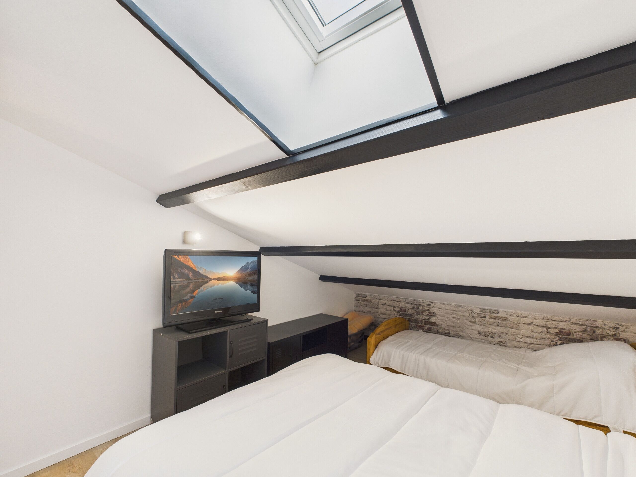 Een moderne slaapkamer met dakraam, een televisie en twee bedden.