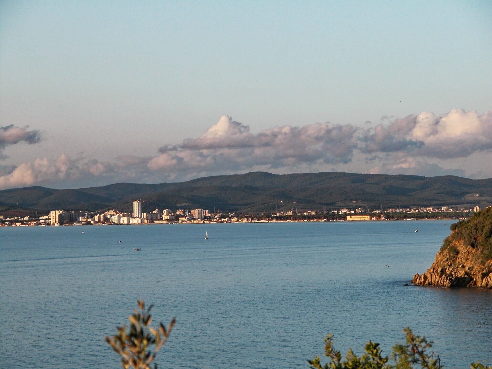 A coastal cityscape with a view of the sea, buildings, and hills in the distance.