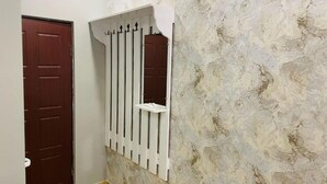 A hallway with a textured wall, a wooden door, and a white window with vertical bars. - Aero Hotel (Parakar)