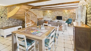 Un espacio habitable amplio con una escalera de madera, paredes de piedra y una mesa de comedor con sillas.