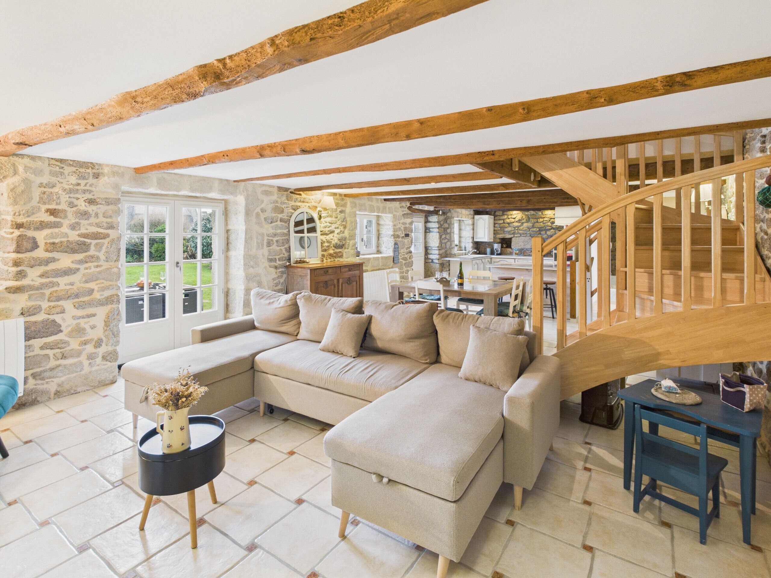 A cozy living room with a stone wall, a wooden staircase, and a large beige sectional sofa.