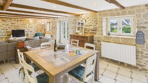 Una habitación acogedora con paredes de piedra, techo de madera, una mesa de comedor con sillas, un sofá y un televisor.