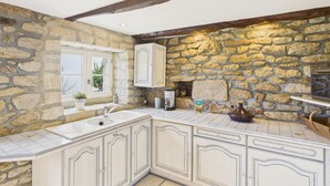 Una cocina con paredes de piedra, muebles blancos y un ventanal con vistas al verdor.