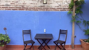 Um pátio com parede azul, duas cadeiras de madeira, uma mesa e um lustre suspenso.