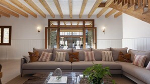 A spacious living room with a large sectional sofa, wooden beams on the ceiling, and a view through glass doors to an outdoor area. - Rural house ORUE BASERRIA in URDAIBAI-with jacuzzi and sauna (Ajuria)