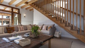 A cozy living room with a wooden staircase, a sofa set, and a coffee table with books and a plant. - Rural house ORUE BASERRIA in URDAIBAI-with jacuzzi and sauna (Ajuria)