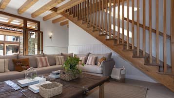 Een gezellige woonkamer met een houten trap, een zithoek en een bijzettafeltje met boeken en een plant.