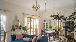 Amplia sala de estar con un sofá color turquesa, comedor con mesa y sillas de madera, y ventanas grandes con cortinas.
