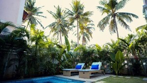 Un área de piscina con sillones de descanso y palmeras.