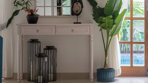 Una habitación con una consola blanca, un espejo grande, una planta en maceta y vistas por una ventana.