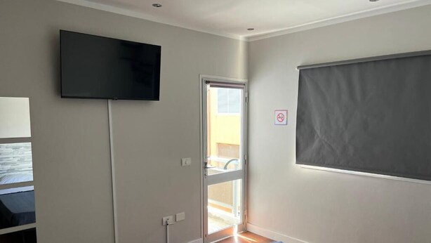 A room with a flat-screen TV mounted on the wall, a sliding door leading to an outdoor area, and a large window with a blind. - B&B paraiso tenerife  (Los Abrigos)