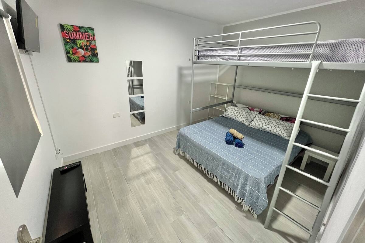 A bunk bed room with a grey floor, a small TV on the wall, and a 'SUMMER' poster.