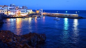 A coastal town at dusk with buildings along the waterfront, a pier, and boats. - B&B paraiso tenerife  (Los Abrigos)