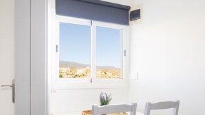 Ein Zimmer mit Fenster und Blick auf eine Landschaft, einem Tisch mit Stühlen und einer Tür.